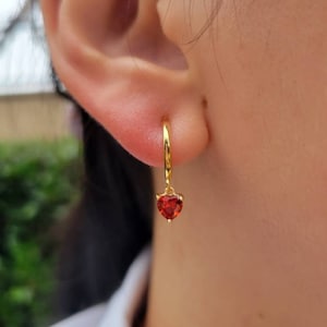 Op de afbeelding: Gouden creolen met een hangende rode hartvormige edelsteen.