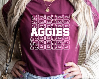 May include: A maroon t-shirt with the word "AGGIES" repeated in a white, outlined, stacked pattern.