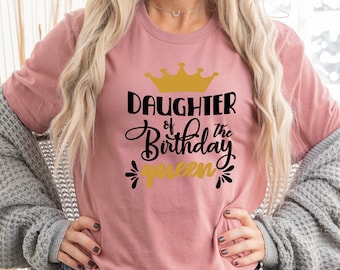 May include: A pink t-shirt with the text "Daughter of the Birthday Queen" in black and gold lettering. The shirt features a gold crown graphic.