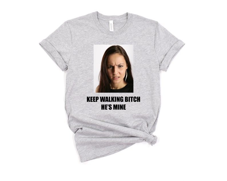 May include: Gray t-shirt with a photo of a woman with a serious expression and the text "KEEP WALKING BITCH HE'S MINE".