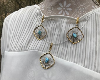 May include: A silver necklace with three gold pendants shaped like trees. Each tree has a blue gemstone in the center.