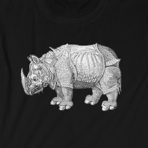 Könnte beinhalten: Schwarzes T-Shirt mit einer weißen Illustration eines Nashorns, das eine Rüstung trägt. Das Nashorn ist nach links gerichtet und hat ein großes Horn auf der Nase.