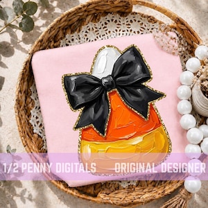May include: A light pink fabric surface featuring a central graphic of a candy corn piece with thick, textured orange and yellow paint strokes, topped with a large black bow and outlined in a shimmering gold glitter border.