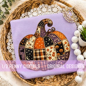 May include: A light purple t-shirt featuring a large, central graphic of a pumpkin constructed from various patchwork fabric patterns, including plaid, stars, moons, leaves, and jack-o'-lanterns, with the text 1/2 PENNY DIGITALS ORIGINAL DESIGNER.