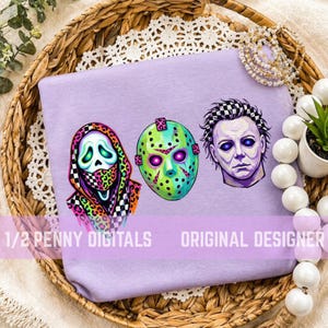 May include: A light purple t-shirt featuring three horror-themed illustrations: a ghost-like figure in a colorful leopard and checkered hood, a green hockey mask with pink accents, and a pale face with dark eyes. Text reads 1/2 PENNY DIGITALS.