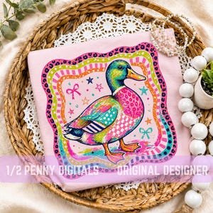 May include: A light pink t-shirt with a vibrant duck design. The duck is depicted with a green head, pink body, and orange feet. The design includes stars, bows, and a rainbow border. The text at the bottom reads "1/2 Penny Digitals Original Designer."