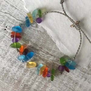 Könnte beinhalten: Ein Regenbogen-Meerglass-Armband mit einem grauen Band und einem verschiebbaren Knotenverschluss.