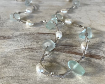 Può includere: Una collana realizzata con perline di vetro blu chiaro e perle bianche, infilate su un cordoncino grigio.