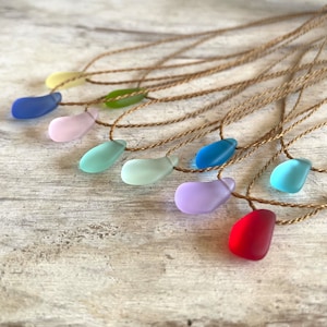 May include: A set of ten necklaces with different colored glass pendants. The necklaces are made with brown cord and the pendants are in shades of blue, green, purple, pink, and red.