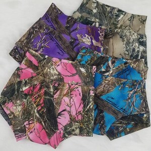 May include: A collection of colorful camouflage shorts in shades of pink, purple, blue, and brown. The shorts feature a ribbed texture and a wide waistband. The camouflage pattern includes tree and leaf designs.