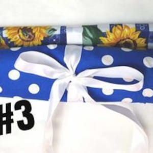 May include: A blue and white polka dot kitchen towel with a white ribbon tied around it. The towel is rolled up and has a wooden dowel rod at each end. The number "#3" is written on the towel.