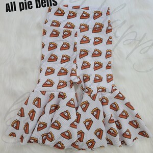 May include: White leggings with a pumpkin pie print and a ruffled hem. The leggings have a split at the bottom.