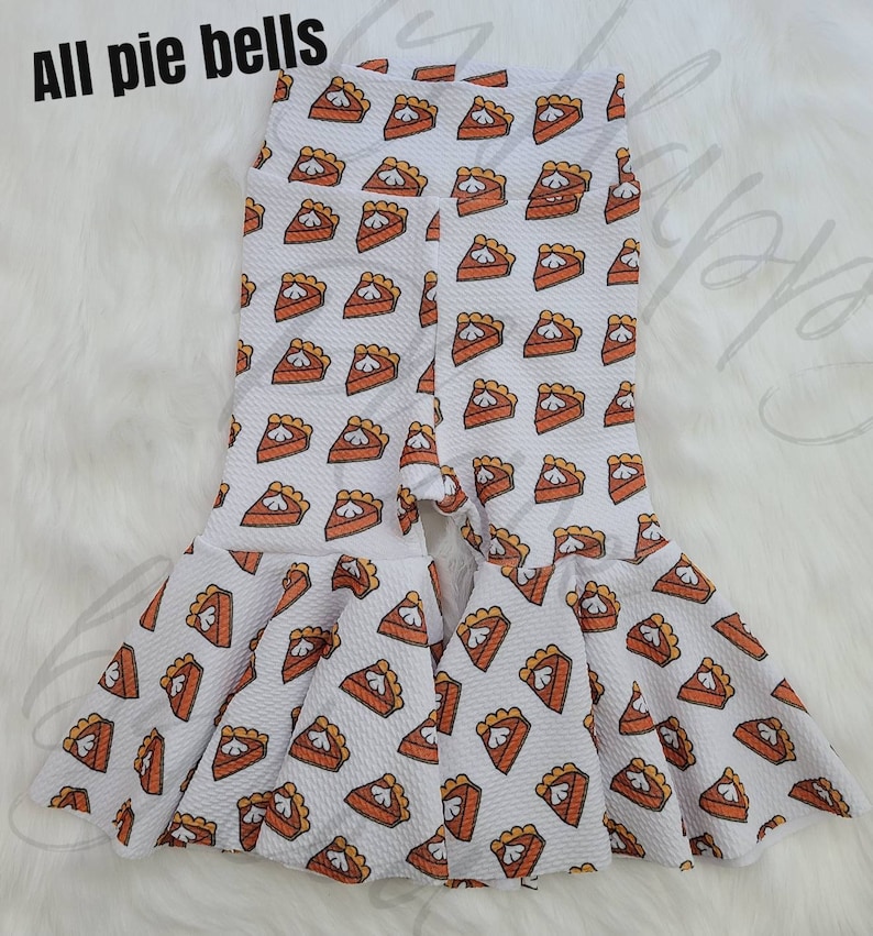 May include: White leggings with a pumpkin pie print and a ruffled hem. The leggings have a split at the bottom.