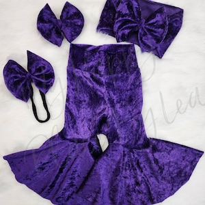 May include: Purple velvet baby outfit with a headband and two bows. The outfit includes a pair of bell bottom pants and a headband with a bow.