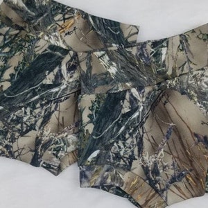 May include: Two pairs of camouflage print shorts. The shorts feature a high waist and are made of a fabric with a pattern of green, brown, and tan hues, resembling a forest environment. The shorts are designed for comfort and style.