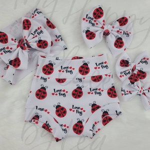 May include: A set of three white fabric headbands with a red ladybug print and the text "Love Bug". The headbands are in different sizes and are perfect for a baby or toddler.