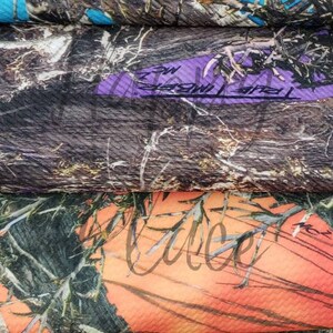 May include: Close-up of several fabric swatches with camouflage patterns. The colors include blue, purple, orange, and various shades of brown and green. Some swatches have text. The fabric has a textured appearance.