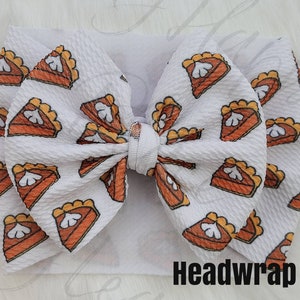 May include: White headband with a large bow made of white fabric with a pumpkin pie print. The text "Headwrap" is printed on the bottom of the image.