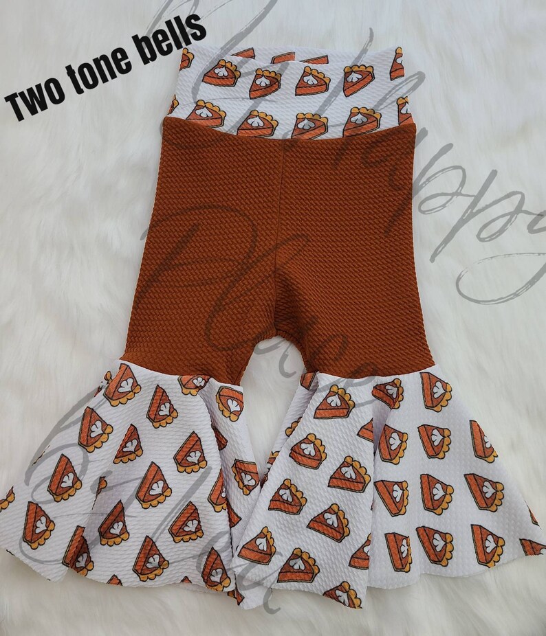 May include: Brown and white bell bottom trousers with a pumpkin pie print. The trousers have a brown waffle knit texture and a white pumpkin pie print on the bottom.