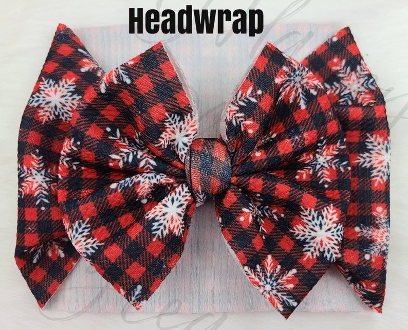 May include: A red and black plaid headwrap with white snowflake accents. The headwrap has a large bow in the center and the word "Headwrap" is printed in black at the top.