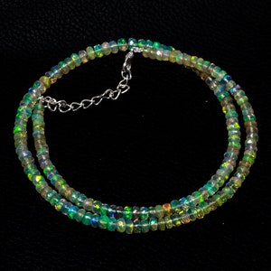 Puede incluir: Un collar compuesto por pequeñas cuentas translúcidas facetadas que muestran destellos iridiscentes de color verde, azul y naranja. La hebra está asegurada con un cierre de mosquetón de metal plateado e incluye una cadena de extensión corta ajustable.