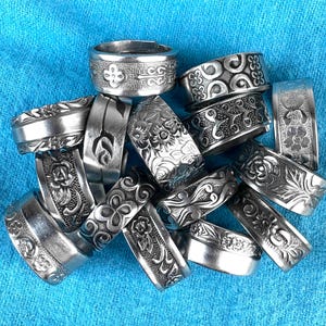 May include: A collection of silver rings with intricate designs. The rings are stacked on top of each other and have a variety of patterns, including floral, geometric, and abstract.