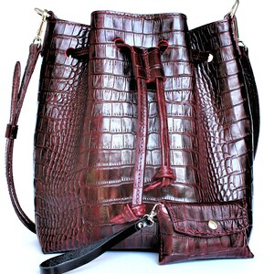 May include: A burgundy leather bucket bag with a drawstring closure and a small matching wallet. The bag has a crocodile embossed pattern.