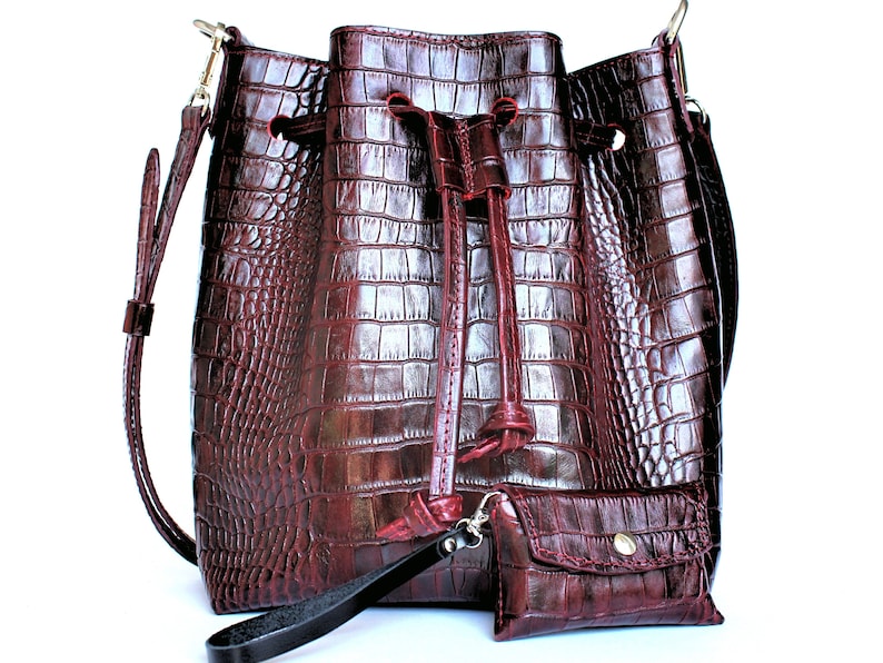 May include: A burgundy leather bucket bag with a drawstring closure and a small matching wallet. The bag has a crocodile embossed pattern.