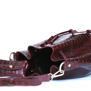May include: A burgundy leather bucket bag with a drawstring closure and a matching small pouch. The bag has a crocodile-embossed pattern.