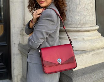 May include: A red leather shoulder bag with a flap closure and a silver buckle. The bag has a brown suede panel on the front.