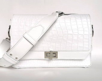 May include: White leather crossbody bag with a crocodile embossed texture and a silver clasp.