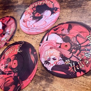 May include: Four vinyl record coasters with anime-style illustrations in shades of red, pink, and black. Each coaster features a different character design and text. The coasters are arranged on a wooden surface.