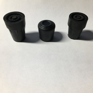 May include: Three black rubber cane tips arranged in a row. The two outer tips feature a wider, reinforced base with a textured exterior, while the center tip is smaller, smooth, and cylindrical with a flat top surface and a circular indentation.