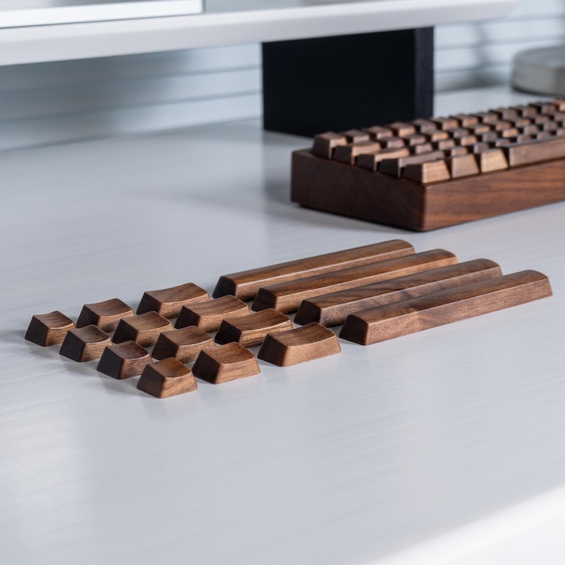 May include: A wooden keyboard with keycaps and long bars. The keycaps are arranged in a cluster, while the bars are aligned horizontally. The keyboard and components are made of dark brown wood, set against a light-colored surface.