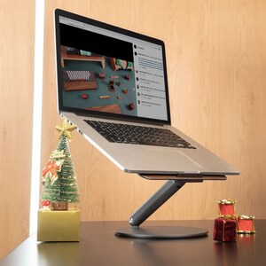 A MacBook sits on a laptop stand with a wooden surface surrounded by Christmas decorations.