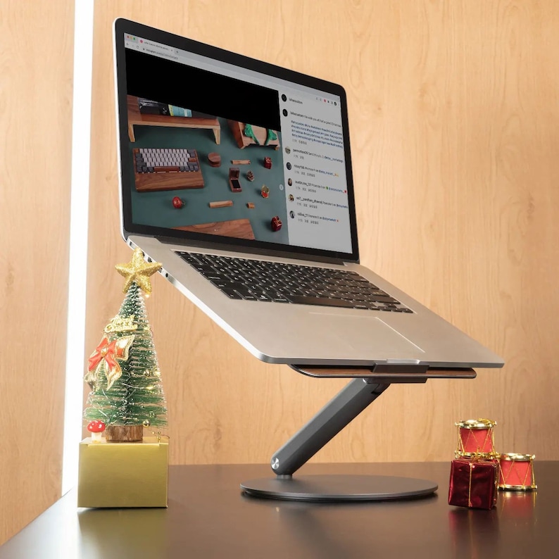 A MacBook sits on a laptop stand with a wooden surface surrounded by Christmas decorations.