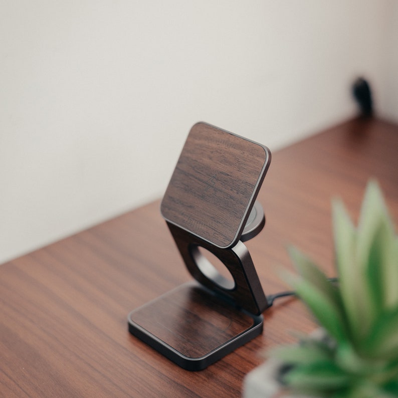 An unrolled 3 in 1 folding charger in walnut color is placed on the table on the walnut table, surrounded by green potted plants, which is very textured.