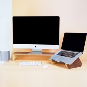 May include: A wooden stand with a desktop computer and a laptop on top. The computer has a black screen and a white keyboard. The laptop has a black screen and a silver keyboard. There is a white mouse and a white keyboard on the desk.