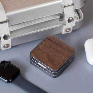 The scene shows a folded 3 in 1 charger, surrounded by a white satchel, Apple Watch and AirPods.