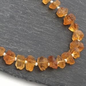 Pu&ograve; includere: Una collana fatta di perline di pietra preziosa arancione e piccole perline bianche. La collana &egrave; su uno sfondo grigio scuro.