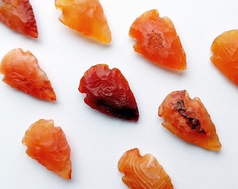 Peut inclure: Dix pointes de flèche en cornaline dans différentes nuances d'orange et de rouge. Les pointes de flèche sont lisses et polies, avec une forme naturelle et organique.
