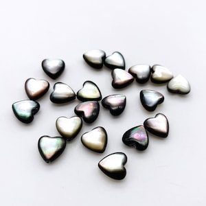 May include: A scattering of iridescent black and white heart-shaped beads. The beads are made of mother of pearl and have a natural, organic look.