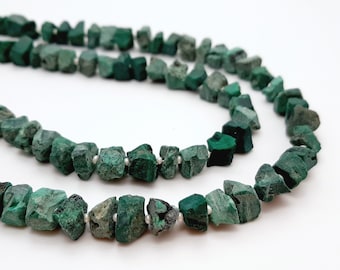 Peut inclure: Un collier de perles de malachite verte, chaque perle est de forme irrégulière et brute. Les perles sont enfilées sur un fil transparent.