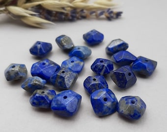 Puede incluir: Una colección de 16 cuentas de piedra preciosa de lapislázuli, cada una con una forma cuadrada facetada. Las cuentas son de color azul intenso con vetas blancas que las atraviesan.