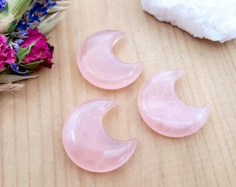 May include: Three pink crescent moon shaped rose quartz crystals on a wooden surface.