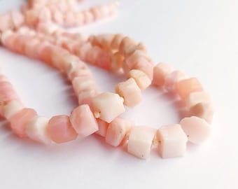 Peut inclure: Un collier de perles d'opale rose, chaque perle est d'une nuance de rose légèrement différente et a une forme légèrement irrégulière. Les perles sont enfilées sur un fil transparent.