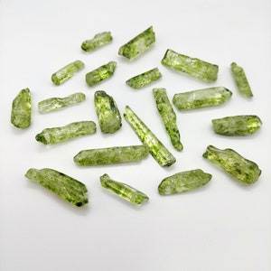 May include: A collection of green and clear crystal points with inclusions. The crystals are various sizes and shapes, and some have a rough texture.