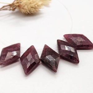 May include: Five faceted, dark pink gemstone beads in a diamond shape. The beads are strung on a clear thread.