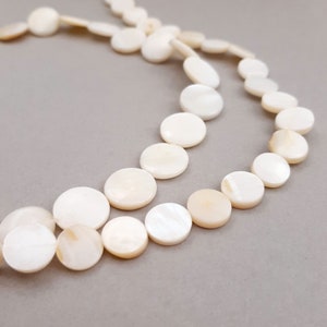 May include: A strand of white mother of pearl beads, each bead is a flat disc shape.