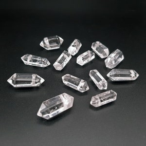 May include: A collection of clear quartz crystal points, also known as double terminated quartz crystals, arranged on a black surface. The crystals are faceted and have a natural, raw appearance.